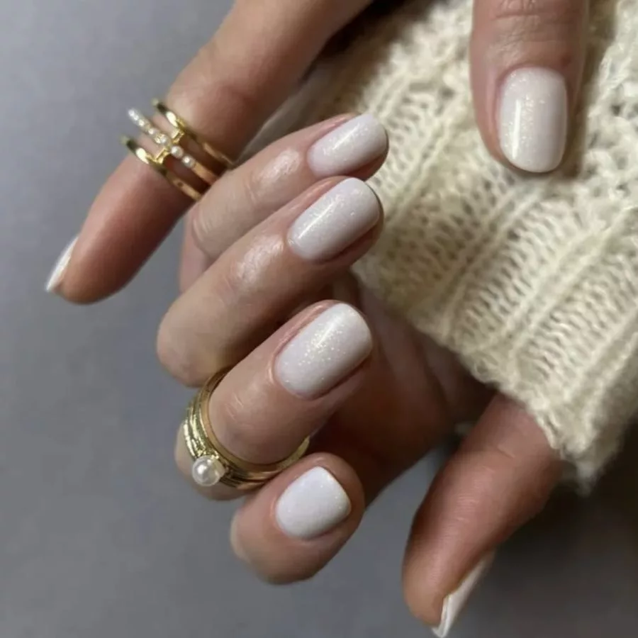 Manucure blanc laiteux shimmer, finition nacrée discrète, bagues or et perle