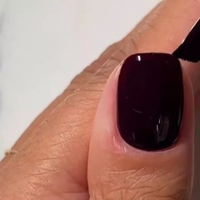 Ongle carré court en cours de pose dans un vernis prune presque noir